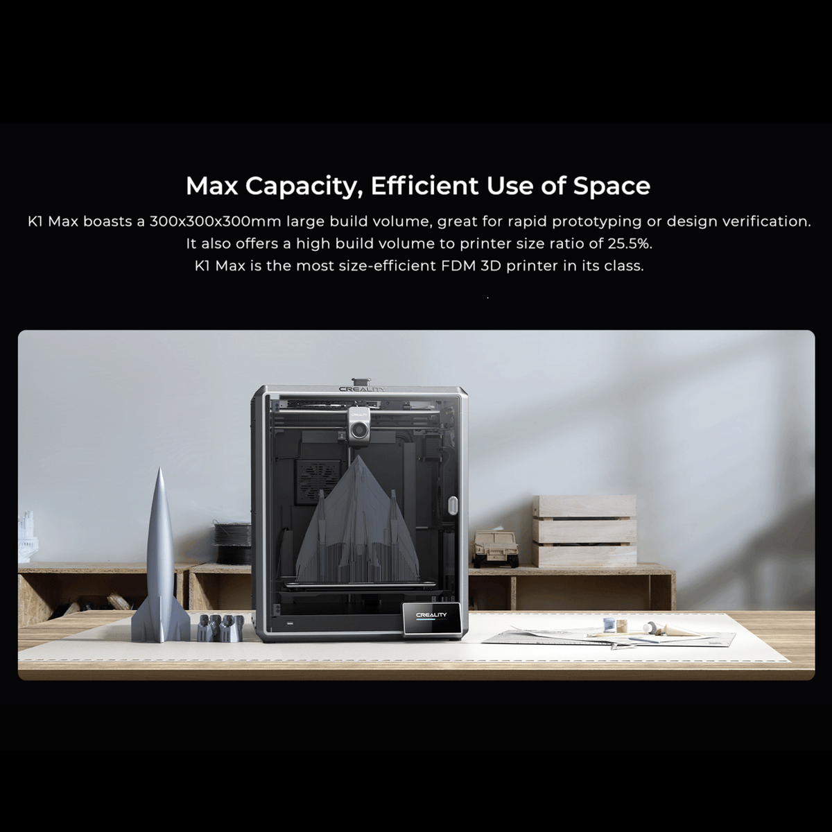 Creality K1 Max 3D printer situated on a design workspace, demonstrating its max capacity and efficient use of space. A large grey rocket model is printing inside the 300x300x300mm large build volume, with a completed replica standing beside it. The scene highlights its 25.5% high build volume to printer size ratio, making it an ideal, size-efficient FDM 3D printer for rapid prototyping and design verification