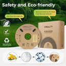 Creality Hyper Series 10mm printer filament spool and its kraft paper packaging box, set against a green outdoor background with text highlighting eco-friendly and safety features.