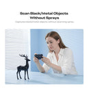 A woman in a white shirt holds a small black device and takes a photo of a black deer figurine on a light blue table. Text above reads 'Scan Black/Metal Objects Without Sprays' with smaller copy below.